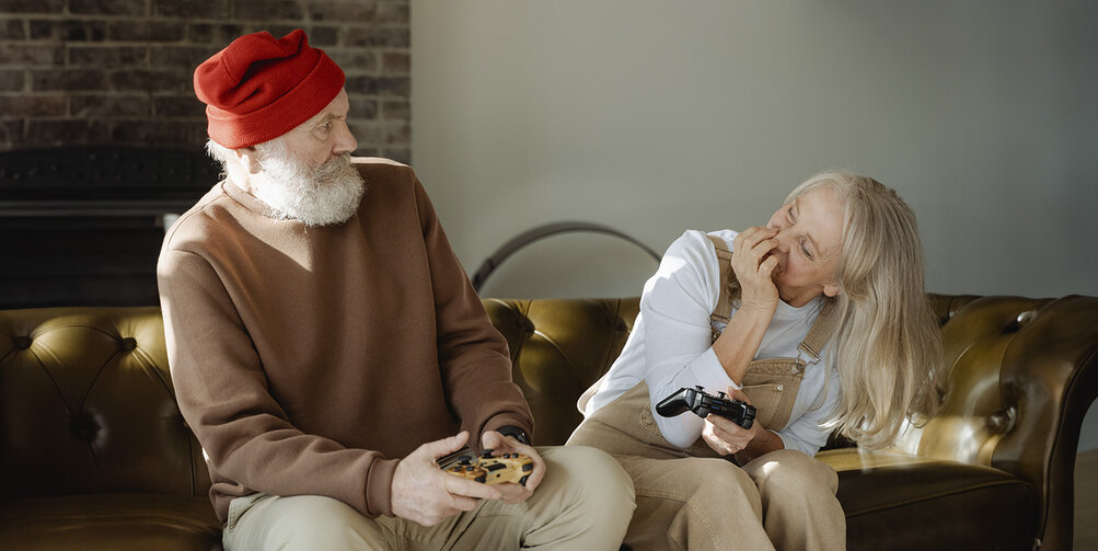 Twee oudere mensen op een bank spelen een game.